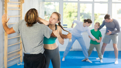 Purposeful engrossed teen girl train during krav maga training session and work out basic elements with male partner. Martial arts school, melee