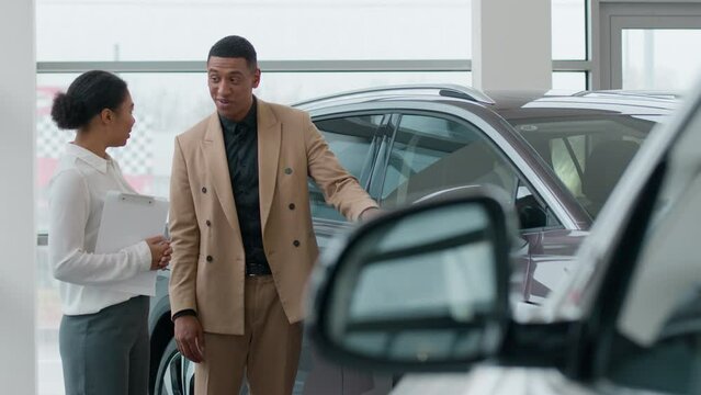 African American woman seller dealer trader consulting in auto showroom help man customer choose new car modern electric automobile saleswoman consult explain vehicle features sale in dealership store