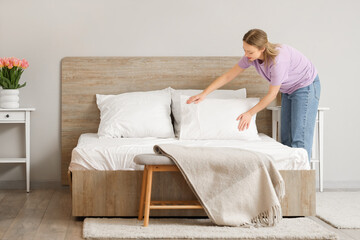 Pretty young woman putting pillow on bed in bedroom