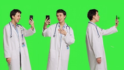 Medic specialist having remote videocall conversation with patients on smartphone internet connection, greenscreen backdrop. Doctor discusses about disease with people on videoconference. Camera B.