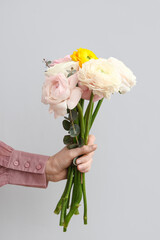 Female hand with beautiful bouquet of ranunculus flowers and eucalyptus on white background