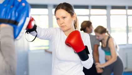 Focused woman in boxing gloves practices punches with man in mitts in gym