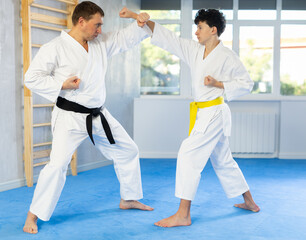 Sportive teenage boy applying blocking and kicking techniques on middle-aged trainer during karate classes