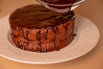A chocolate cake with chocolate drizzle on top is being poured onto a white plate. The cake is sitting on a countertop