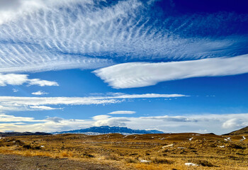 Altocumulus clouds and other cloud formations in deep blue sky hover over Absaroka Mountains in...