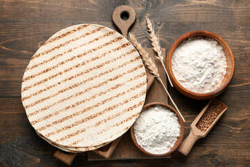 Fresh lavash and bowls of flour on wooden background