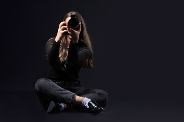 Female photographer with modern camera taking picture of viewer on black background