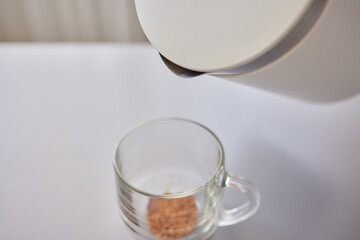 Woman stirs instant coffee in glass mug with boiled water on grey stone table