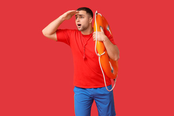Worried young lifeguard with whistle and lifebuoy looking at somewhere on red background