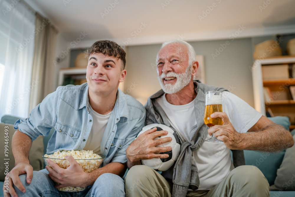 Wall mural teenager and his grandfather senior man watch football game at home