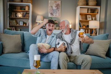 teenager and his grandfather senior man watch football game at home