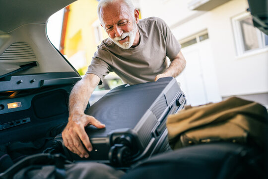 One senior man travel concept male put suitcase in trunk of the car - Powered by Adobe