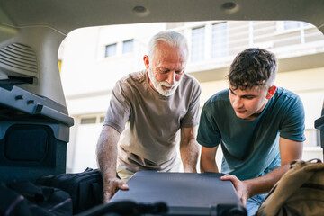 Two men Teenager and senior grandfather pack baggage in trunk of car