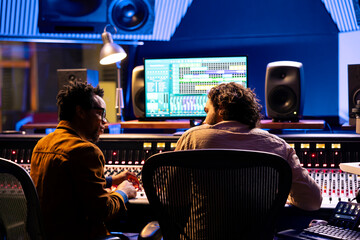 Team of sound technician and singer working on new music, mixing tunes on digital software in...