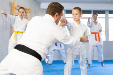 Boy train and learn during family group lesson in oriental martial arts. Man teacher corrects pose posture position of body, hands during karate classes. © JackF