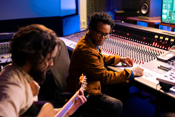 Artist playing a new record on his guitar in control room, recording and producing music with audio...