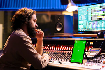 Skilled sound engineer looks at mockup display on tablet before mixing and mastering tracks on...