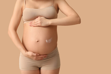 Young pregnant woman with cream against stretch marks on beige background