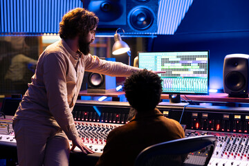 Skilled musician working with audio engineer to edit new recorded tracks in control room, pressing...