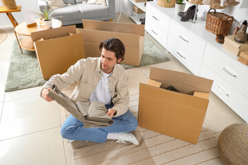 Handsome young man unpacking wardrobe boxes with stylish clothes in dressing room