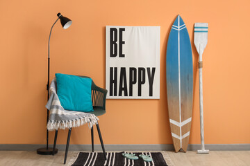 Surfboard, picture, armchair and paddle near orange wall in room