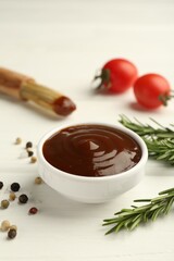 Tasty barbeque sauce in bowl, rosemary and spices on white wooden table