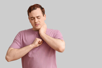 Young man with sore throat on light background