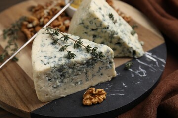 Tasty blue cheese with thyme, honey and walnuts on wooden board, closeup