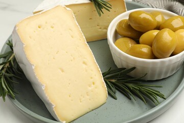 Plate with pieces of tasty camembert cheese, olives and rosemary on white table, closeup