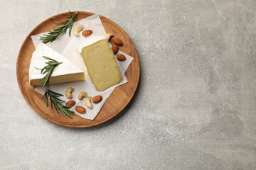 Plate with pieces of tasty camembert cheese, nuts and rosemary on grey textured table, top view....