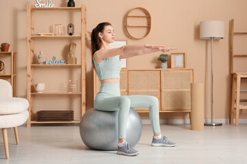 Fototapeta premium Beautiful young sporty woman with fitness ball training at home