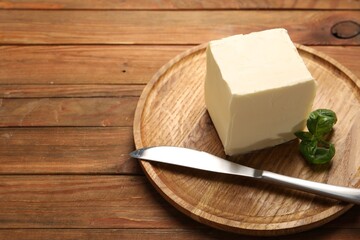 Block of tasty butter, knife and basil on wooden table. Space for text