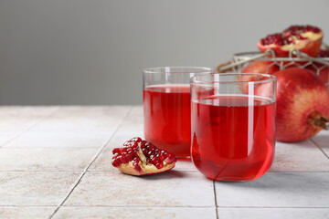 Tasty pomegranate juice in glasses and fresh fruits on white tiled table. Space for text