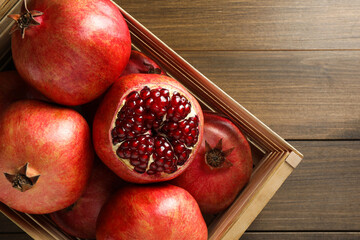 Ripe pomegranates in crate on wooden table, top view