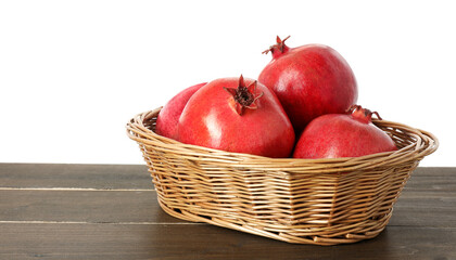 Fresh pomegranates in wicker basket on wooden table against white background