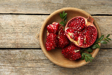 Cut fresh pomegranate and green leaves on wooden table, top view. Space for text