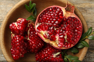 Cut fresh pomegranate and green leaves on wooden table, top view