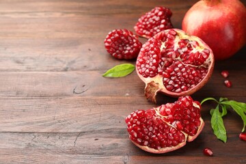 Fresh pomegranates and green leaves on wooden table, space for text