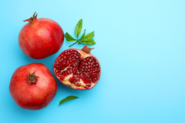 Fresh pomegranates and green leaves on light blue background, flat lay. Space for text