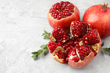 Fresh pomegranates and green leaves on grey textured table, space for text