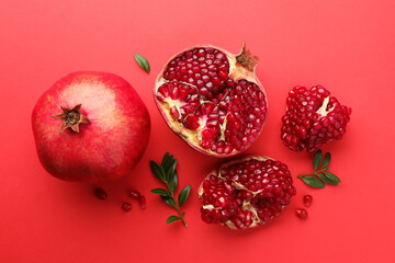 Fresh pomegranates and green leaves on red background, flat lay