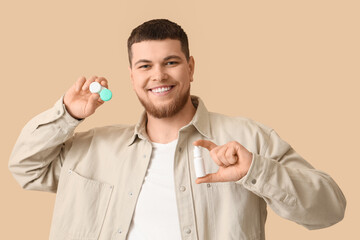 Young man with contact lenses and eye drops on beige background