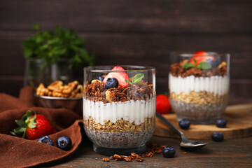 Tasty granola with berries, yogurt and chia seeds in glass on wooden table