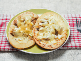 Meal with two pita bread with chopped cooked chicken fillet and melted cheese on a green plate and light color table clothes. Pizza style dish. Quick lunch.