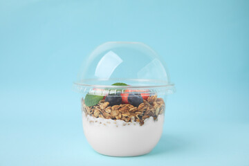 Tasty granola with berries and yogurt in plastic cup on light blue background