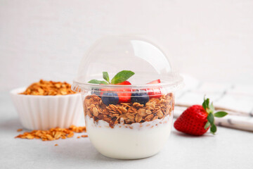Tasty granola with berries and yogurt in plastic cup on light table
