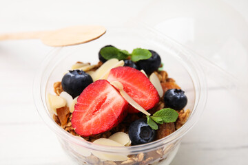Tasty granola with berries, almond flakes and mint in plastic cup on white table, closeup