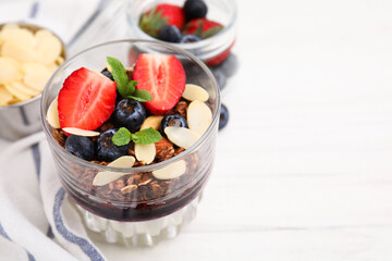 Tasty granola with berries, jam, yogurt and almond flakes in glass on white table, closeup. Space for text