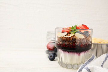 Tasty granola with berries, jam, yogurt and almond flakes in glass on white table. Space for text