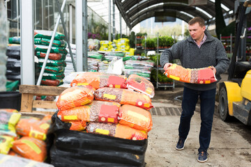 serious male worker unloading garden substrates in gardening store
